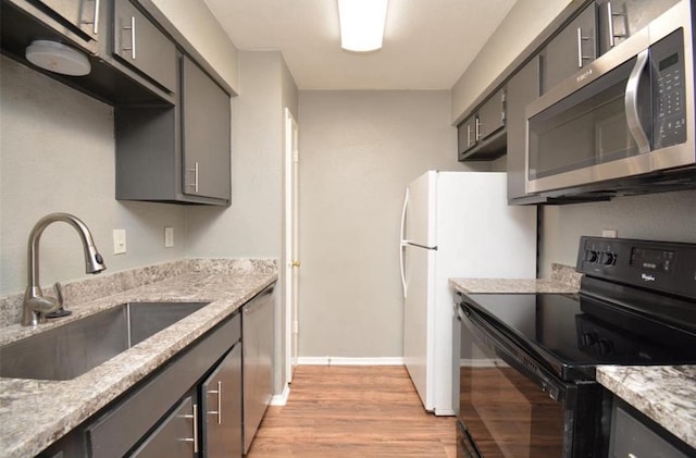 kitchen featuring gray cabinets, appliances with stainless steel finishes, a sink, baseboards, and light wood-style flooring