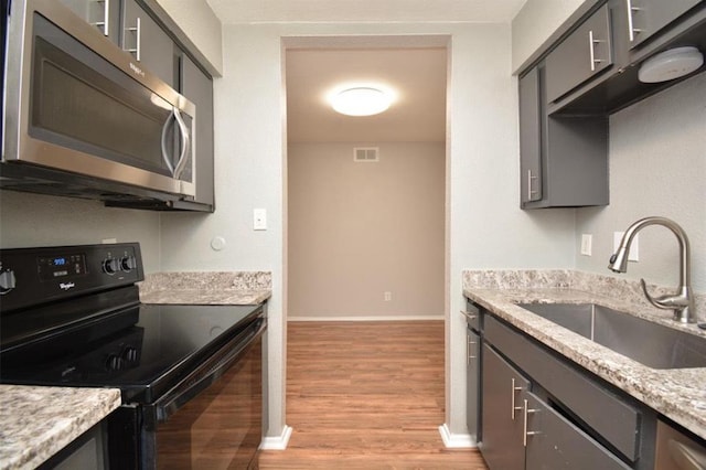 kitchen featuring visible vents, black electric range oven, light wood-type flooring, stainless steel microwave, and a sink