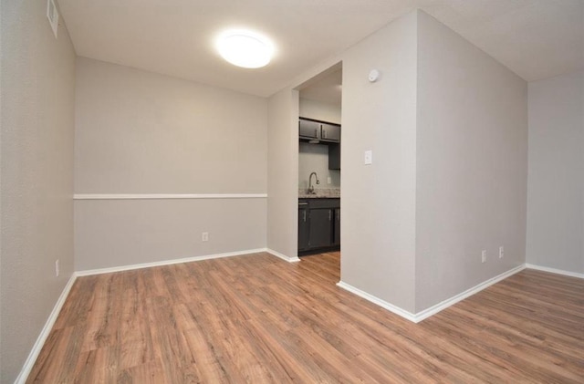 empty room featuring light wood-style floors, baseboards, and a sink