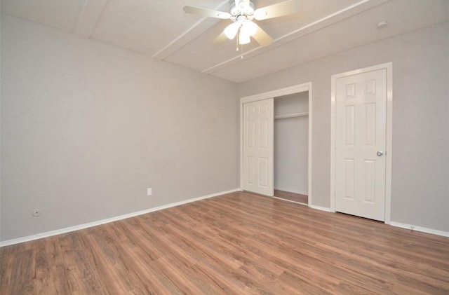 unfurnished bedroom featuring baseboards, a ceiling fan, wood finished floors, and a closet