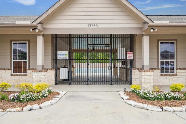 property entrance with roof with shingles, fence, a gate, and stone siding