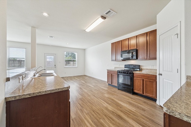 kitchen featuring a sink, light wood finished floors, black appliances, and light countertops