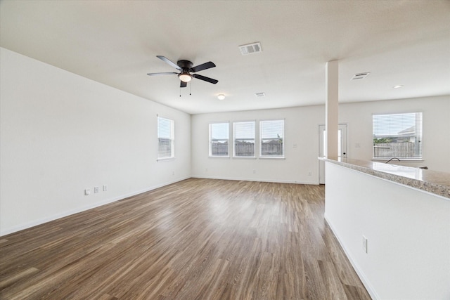 empty room featuring plenty of natural light, ceiling fan, wood finished floors, and visible vents