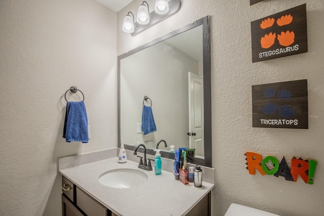 half bath with vanity, a textured wall, and toilet