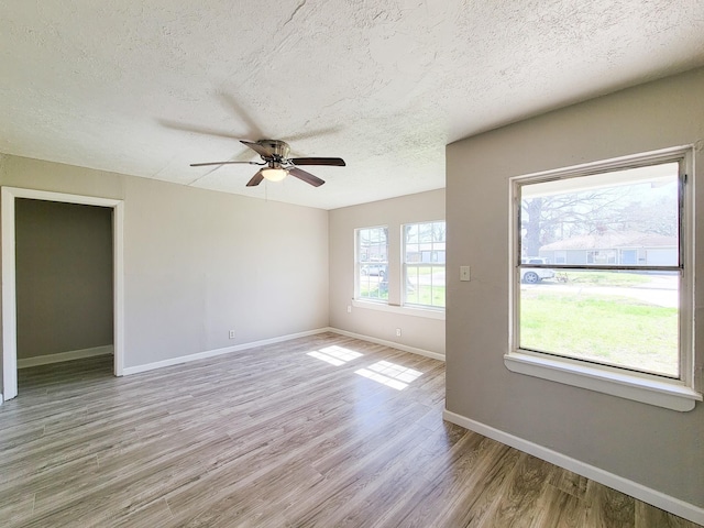 empty room featuring a ceiling fan, a textured ceiling, baseboards, and light wood finished floors
