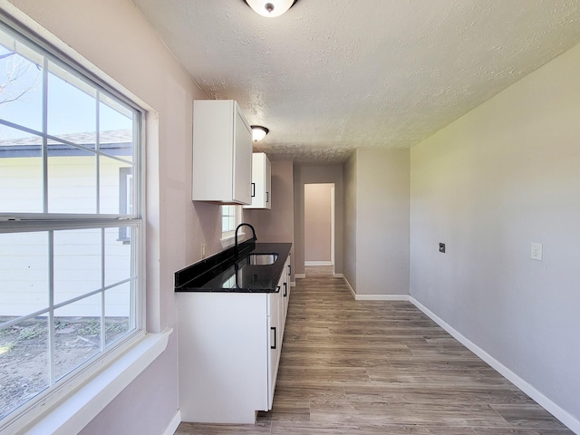 kitchen featuring a textured ceiling, dark countertops, a sink, baseboards, and white cabinetry