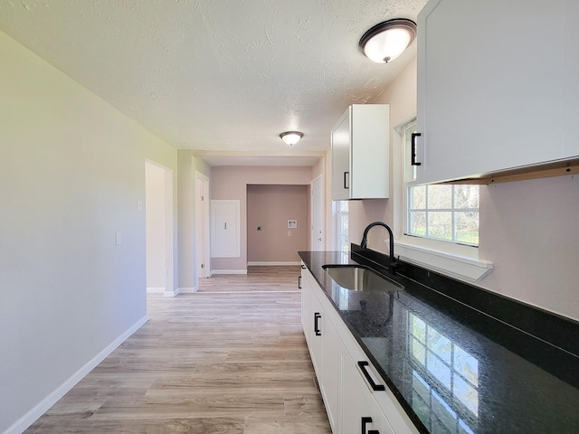 kitchen with white cabinets, a textured ceiling, a sink, and dark stone countertops