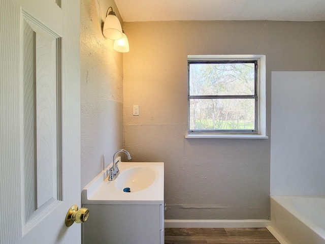 full bathroom with baseboards, a bathing tub, vanity, and wood finished floors