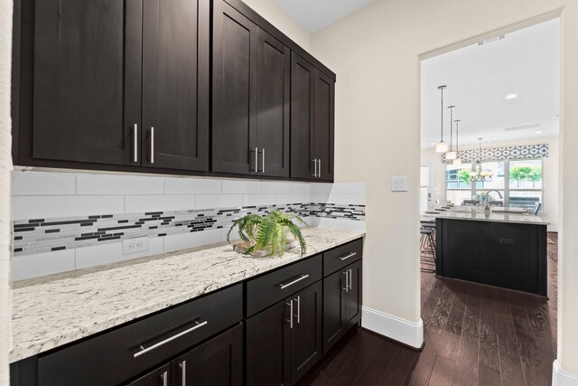 kitchen featuring baseboards, dark wood-style floors, a chandelier, light stone counters, and backsplash