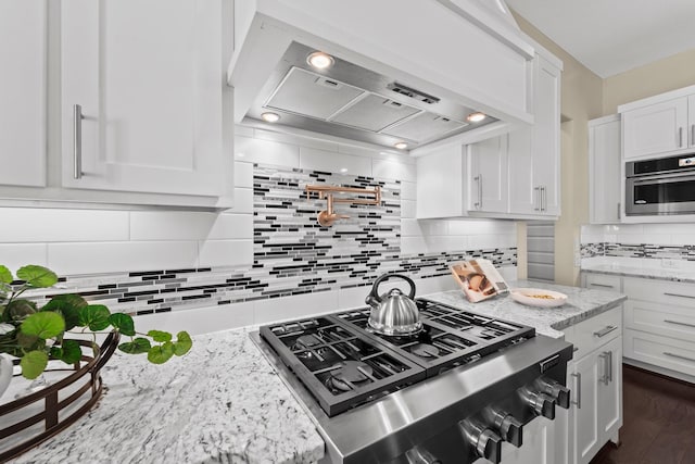 kitchen with wall chimney range hood, white cabinetry, light stone counters, appliances with stainless steel finishes, and backsplash