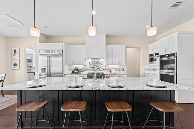 kitchen with decorative light fixtures, visible vents, a large island with sink, stainless steel appliances, and white cabinetry
