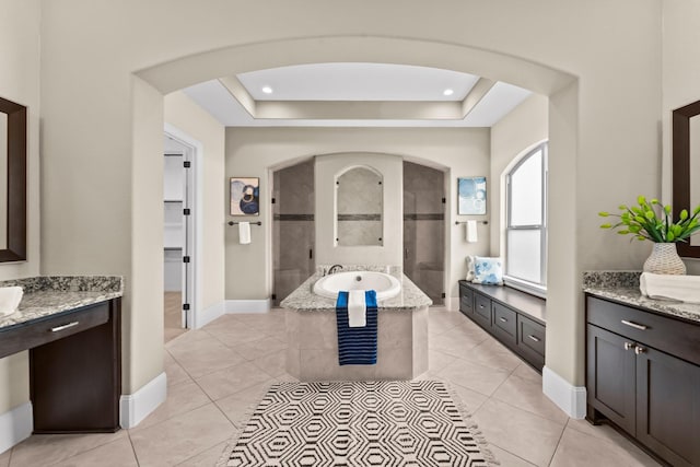 full bathroom featuring a walk in shower, a raised ceiling, a garden tub, and two vanities