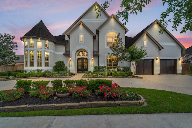 french country inspired facade featuring fence, an attached garage, stucco siding, french doors, and driveway