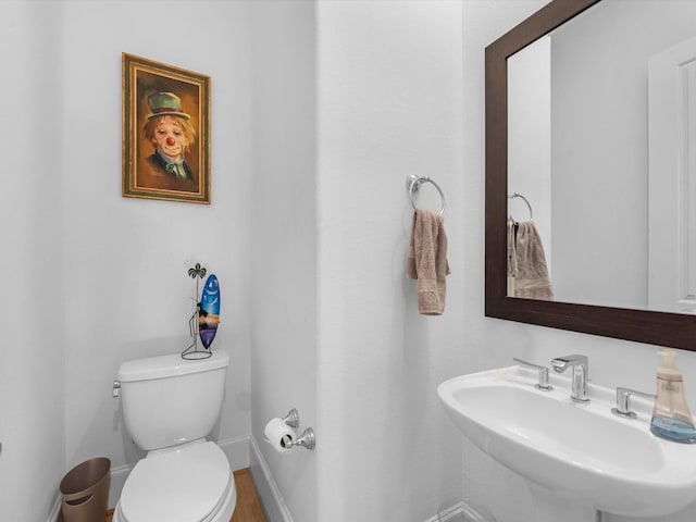 half bath with baseboards, a sink, and toilet