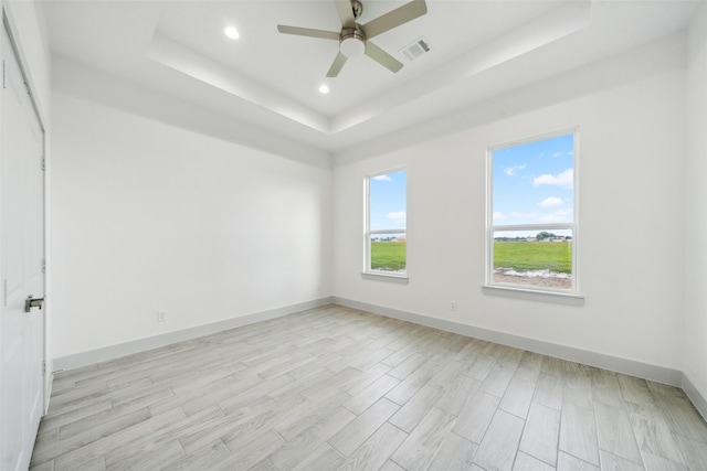 empty room featuring ceiling fan, visible vents, light wood-type flooring, a tray ceiling, and recessed lighting