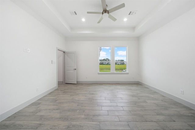 unfurnished bedroom with recessed lighting, a tray ceiling, visible vents, and light wood finished floors