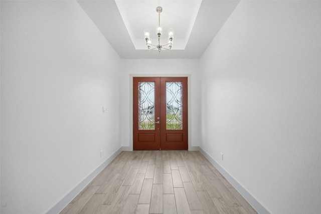 entrance foyer featuring a raised ceiling, baseboards, light wood finished floors, and a notable chandelier
