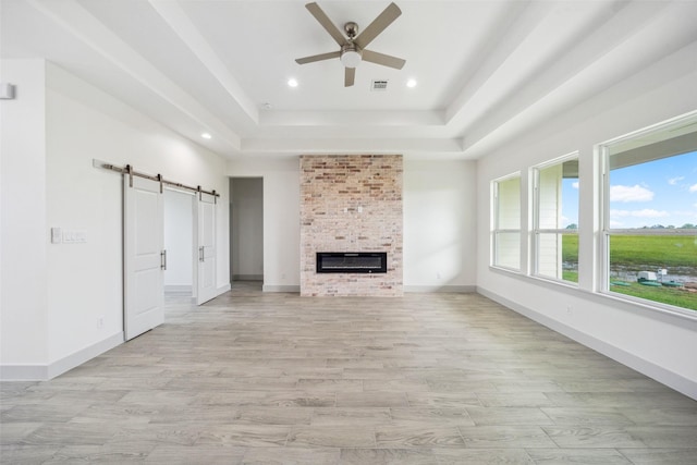 unfurnished living room featuring ceiling fan, a barn door, a raised ceiling, light wood-style flooring, and recessed lighting