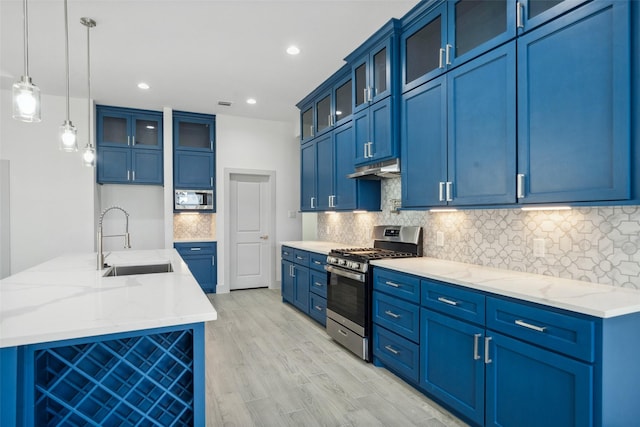 kitchen with light stone countertops, under cabinet range hood, a sink, light wood-style flooring, and appliances with stainless steel finishes