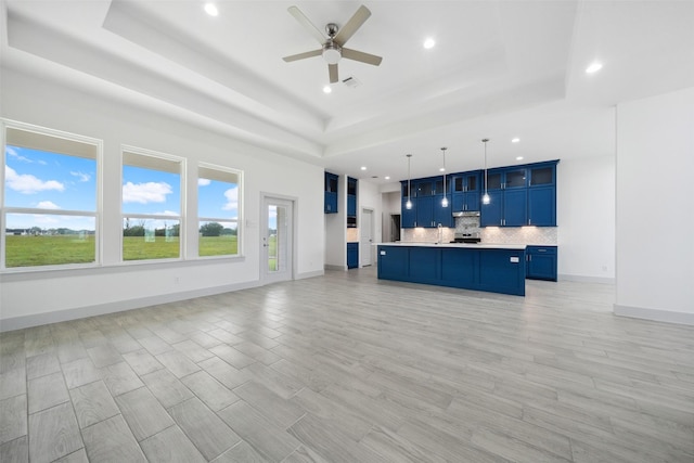unfurnished living room with recessed lighting, a ceiling fan, a tray ceiling, and light wood-type flooring
