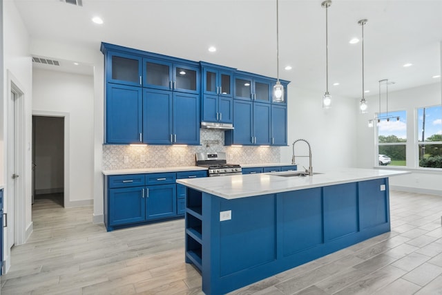 kitchen with gas stove, a sink, light wood-style floors, blue cabinetry, and tasteful backsplash