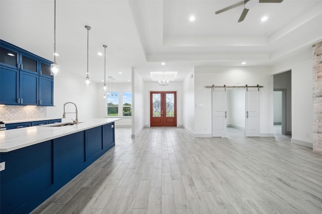 interior space with ceiling fan, a barn door, a raised ceiling, a sink, and blue cabinetry