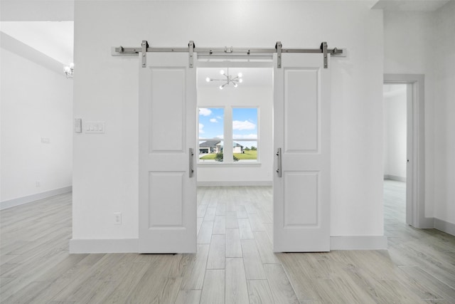 interior space with baseboards, a chandelier, a barn door, and light wood finished floors