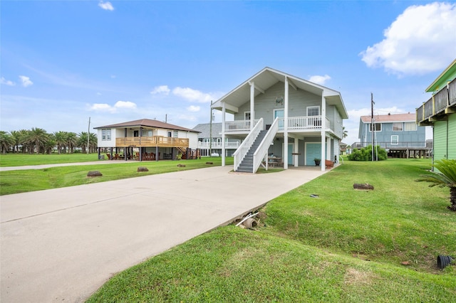 coastal home with concrete driveway, covered porch, stairs, and a front yard