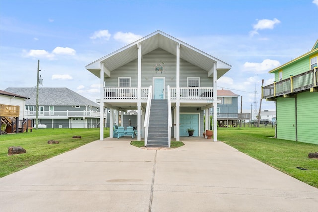 coastal inspired home with covered porch, a garage, stairway, a front lawn, and concrete driveway