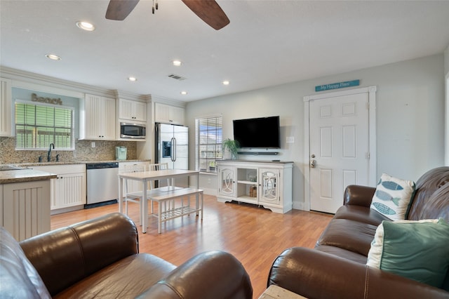 living room featuring light wood-style floors, a ceiling fan, a wealth of natural light, and visible vents