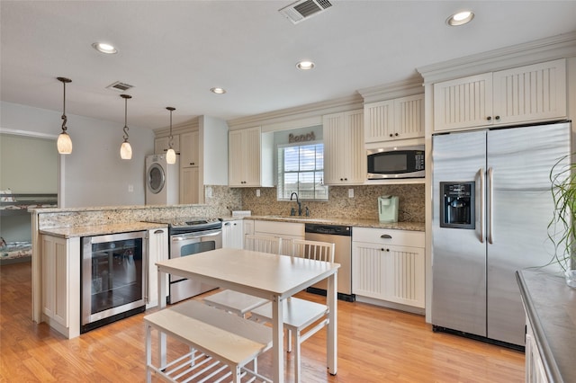 kitchen with stainless steel appliances, a peninsula, wine cooler, visible vents, and stacked washer and clothes dryer