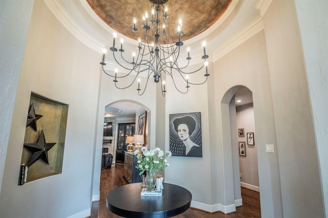 corridor with crown molding, dark wood-type flooring, a tray ceiling, arched walkways, and a notable chandelier
