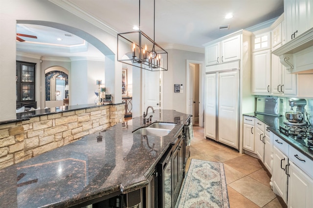 kitchen with a sink, arched walkways, crown molding, and white cabinetry