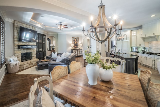dining area with a stone fireplace, arched walkways, ceiling fan with notable chandelier, and ornamental molding