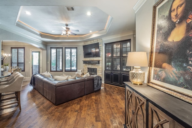 living area with arched walkways, plenty of natural light, a ceiling fan, and a stone fireplace