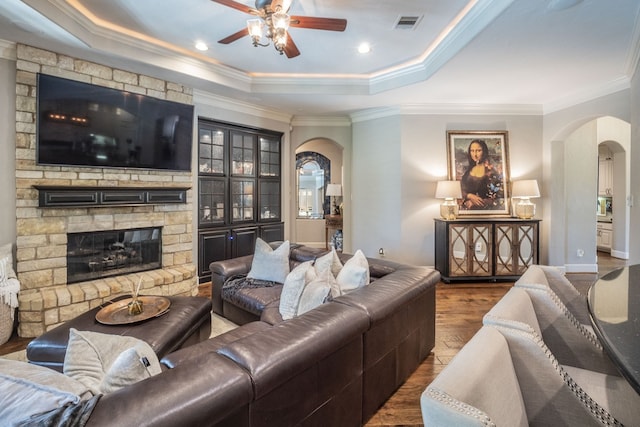living area with ceiling fan, arched walkways, a fireplace, wood finished floors, and a tray ceiling