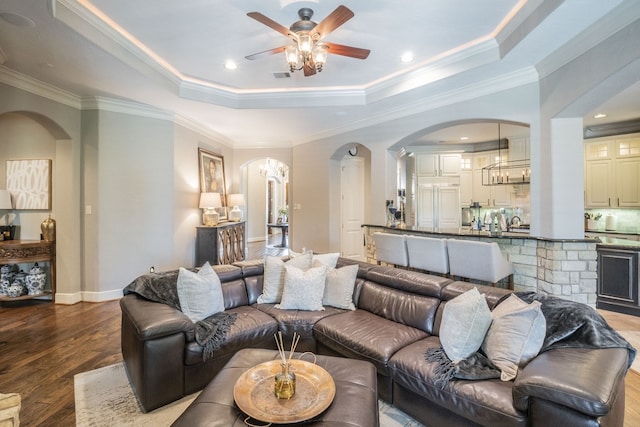 living area featuring ceiling fan, a raised ceiling, arched walkways, wood finished floors, and visible vents