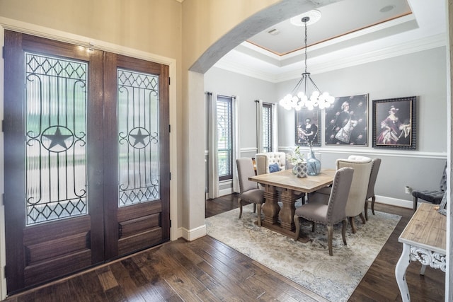 foyer entrance with crown molding, arched walkways, a chandelier, a tray ceiling, and dark wood-type flooring