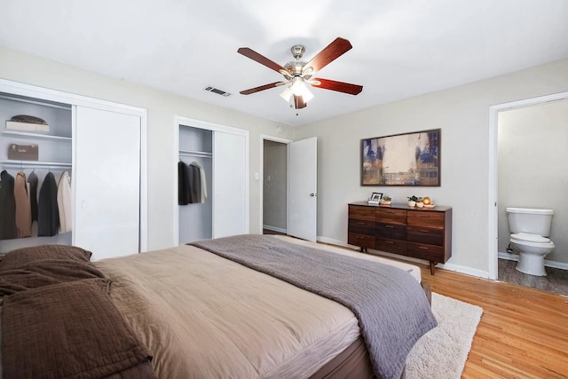 bedroom featuring connected bathroom, multiple closets, baseboards, wood finished floors, and visible vents