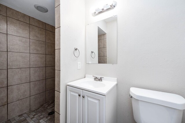 full bathroom with vanity, a tile shower, and toilet