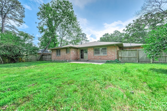 rear view of property with brick siding, a fenced backyard, a patio area, and a lawn