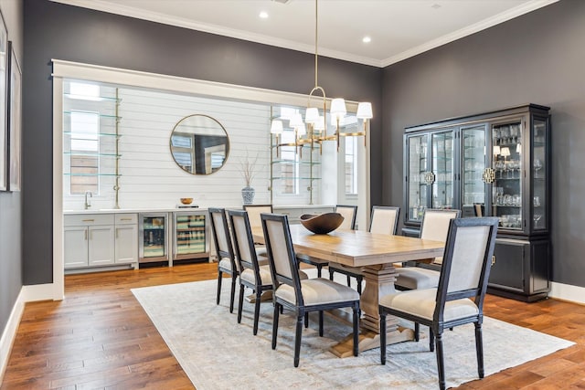 dining area featuring a chandelier, baseboards, wood finished floors, wine cooler, and ornamental molding