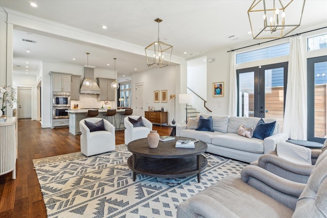 living area with stairway, an inviting chandelier, dark wood finished floors, and visible vents