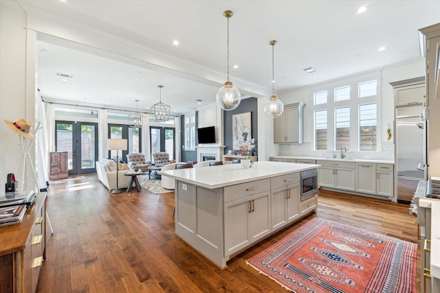 kitchen with gray cabinets, a kitchen island, a sink, light countertops, and built in appliances