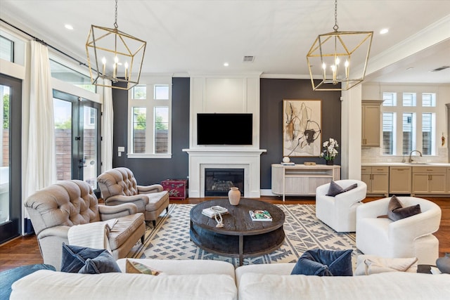 living area featuring an inviting chandelier, ornamental molding, wood finished floors, and a fireplace