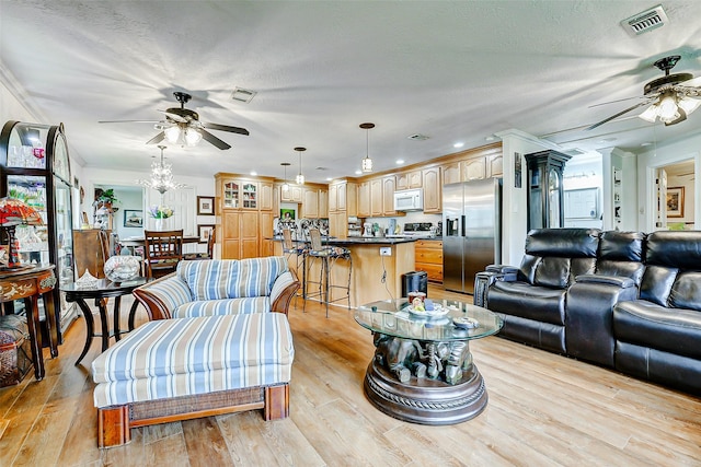 living area featuring light wood-style floors, a ceiling fan, and visible vents
