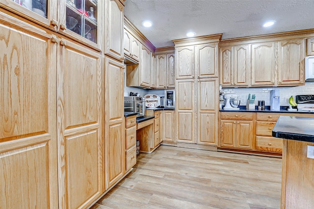 kitchen with light brown cabinetry, dark countertops, white microwave, and light wood-style flooring