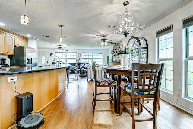 dining space featuring light wood-style floors, a textured ceiling, ceiling fan with notable chandelier, and a wealth of natural light