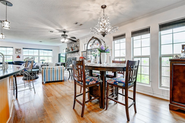 dining room featuring visible vents, a stone fireplace, light wood-style flooring, and ceiling fan with notable chandelier
