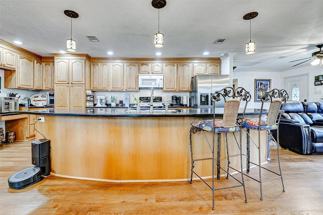 kitchen featuring stainless steel appliances, open floor plan, dark countertops, and light wood-style floors